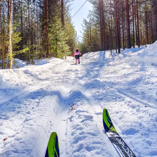 Barn som åker skidor i vit snö med strålande sol.